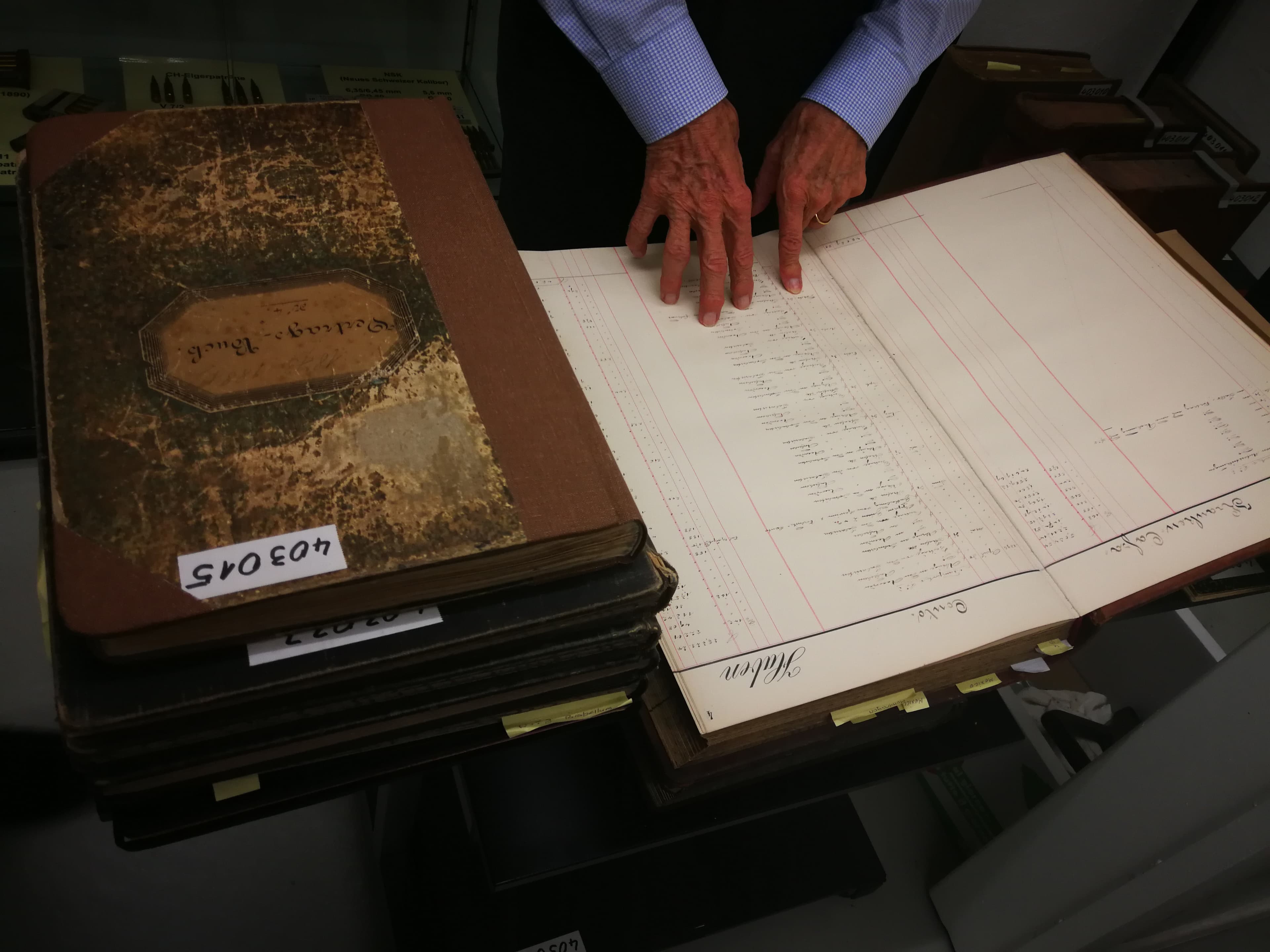 Riesige, handgeschriebene Bücher aus dem Archiv. In dem aufgeschlagenen Buch liest man über die firmeneigene Krankenkasse, unter anderem.
